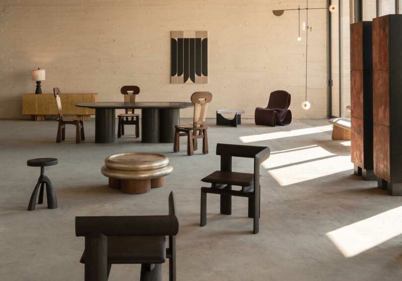 Minimalist loft interior with eclectic modern furniture, including dark wood chairs, round tables, a sculptural armchair, abstract wall art, and soft natural lighting.