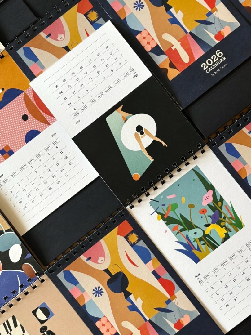 A 2026 spiral-bound calendar with abstract and colorful illustrations is displayed open, showing various monthly pages and cover designs
