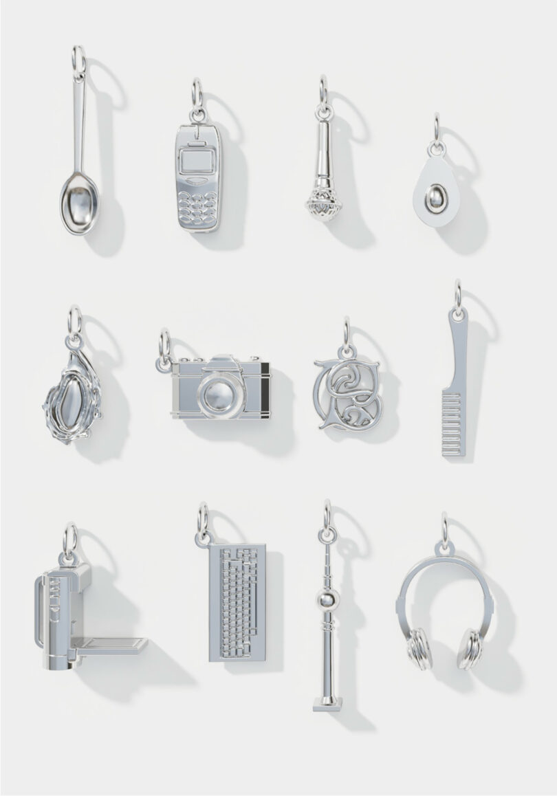 Twelve silver charms shaped like a spoon, cell phone, microphone, teardrop, mirror, camera, letters, comb, electric kettle, keyboard, key, and headphones on a white background.