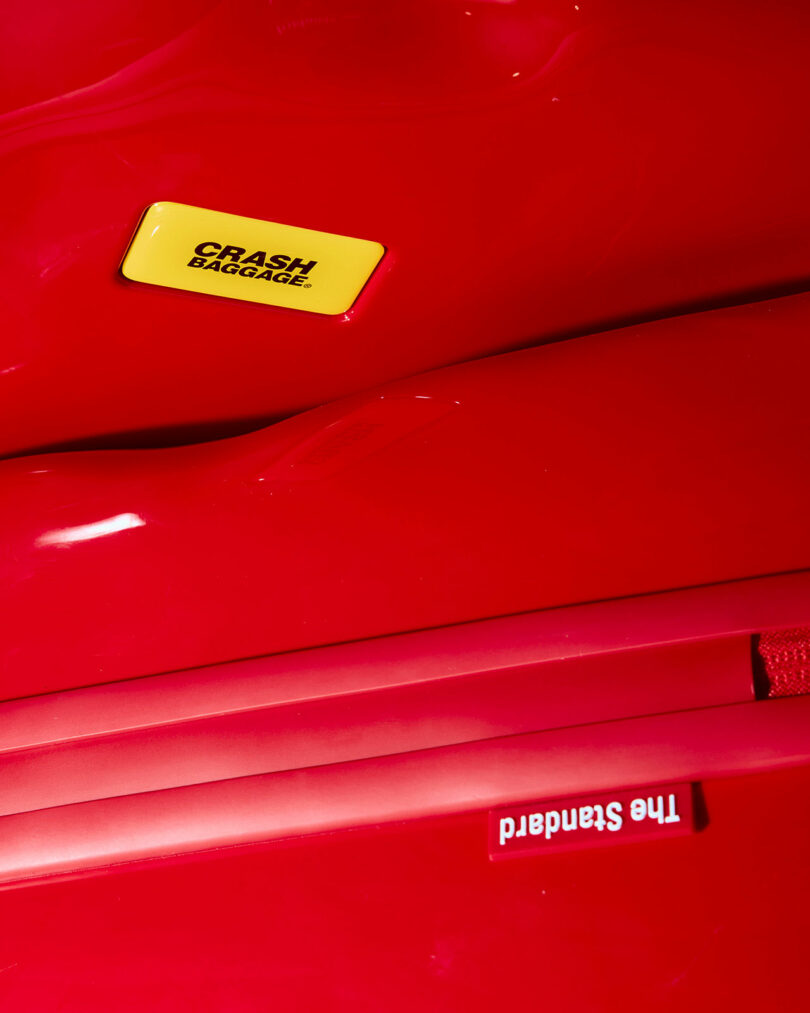 Close-up of two red suitcases—one featuring a yellow "CRASH BAGGAGE" label, showcasing the bold Crash Baggage style, and another with a red label reading "The Standard.