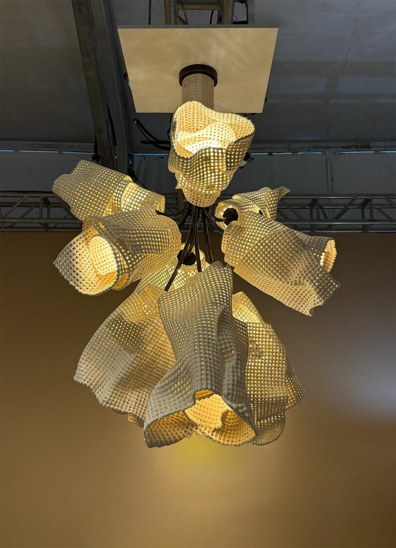 A modern chandelier with multiple sculpted, perforated lampshades emitting warm light, suspended from a ceiling in an indoor setting.