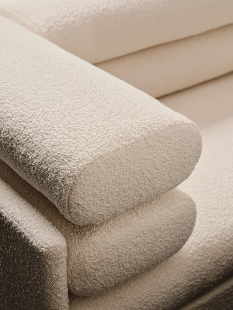 Close-up of a beige textured fabric sofa with rounded armrests and overlapping cushions.