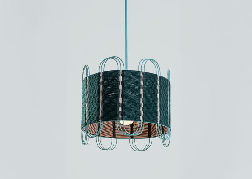 A modern pendant light with a cylindrical shade, textured dark material, and decorative wire loops—designed by Laura Casañas Maya—hangs elegantly from the ceiling on a single cord.
