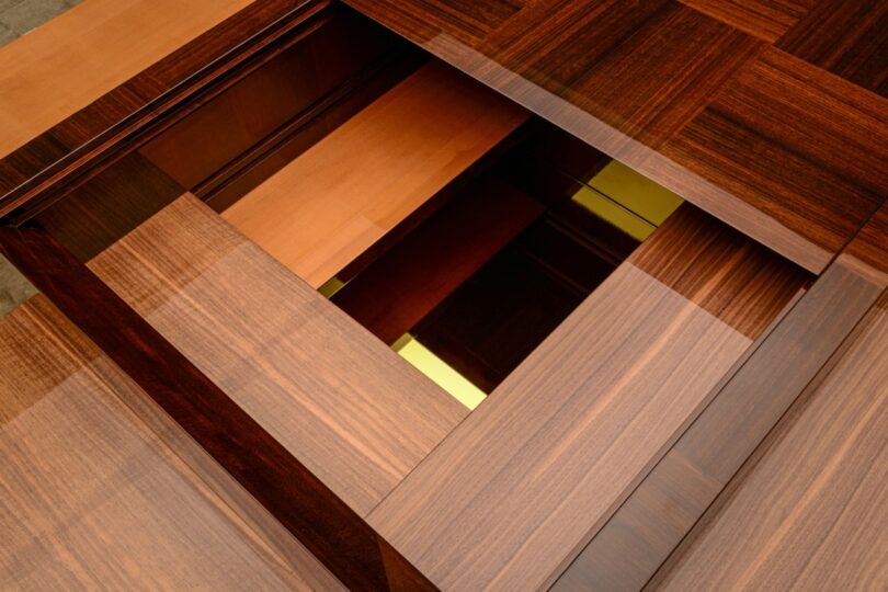Close-up view of a geometric wooden structure with overlapping panels, revealing a recessed section with gold and lighter wood accents