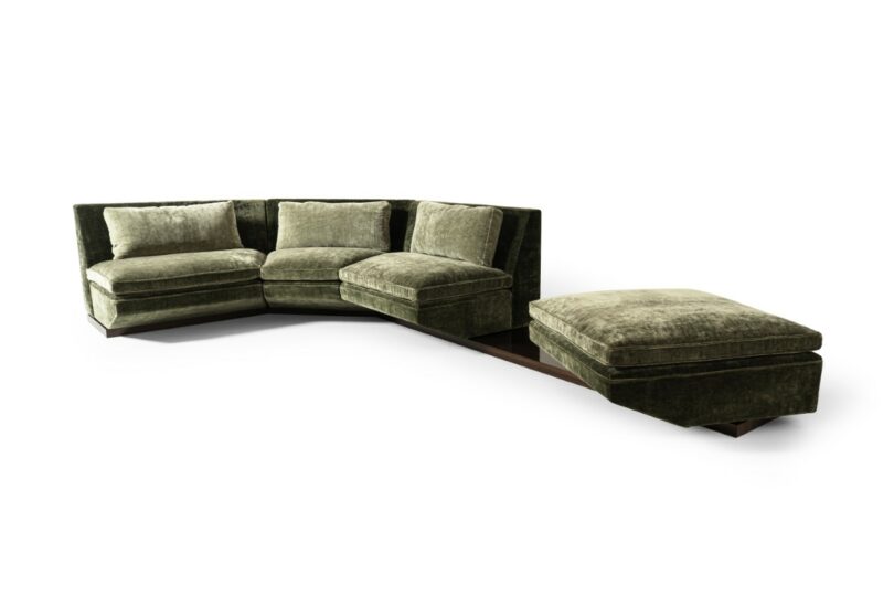 Green velvet sectional sofa with three seats, an attached wooden side table, and a matching ottoman, all set against a white background.