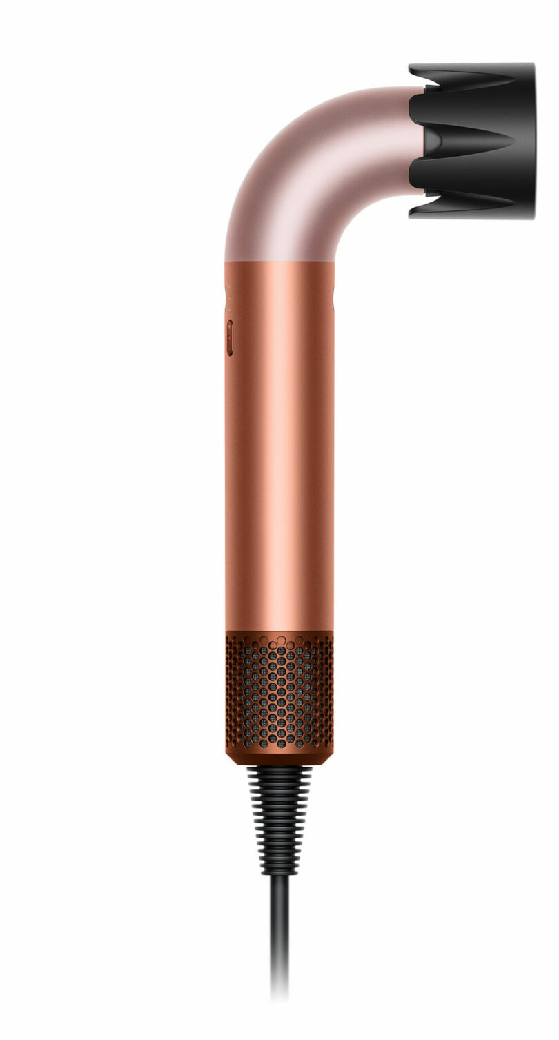 A modern hair dryer with a metallic copper finish is shown in a side profile view with a black nozzle attachment and a visible power cord.