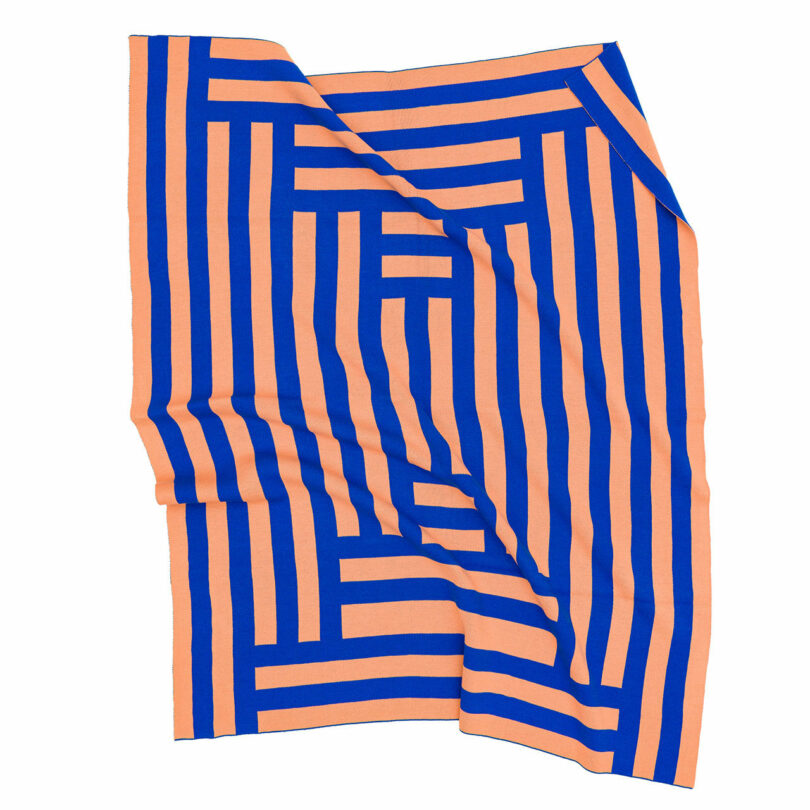 A rectangular textile features a geometric maze-like pattern in blue and peach, with bold lines creating interlocking shapes. The fabric is slightly rumpled.
