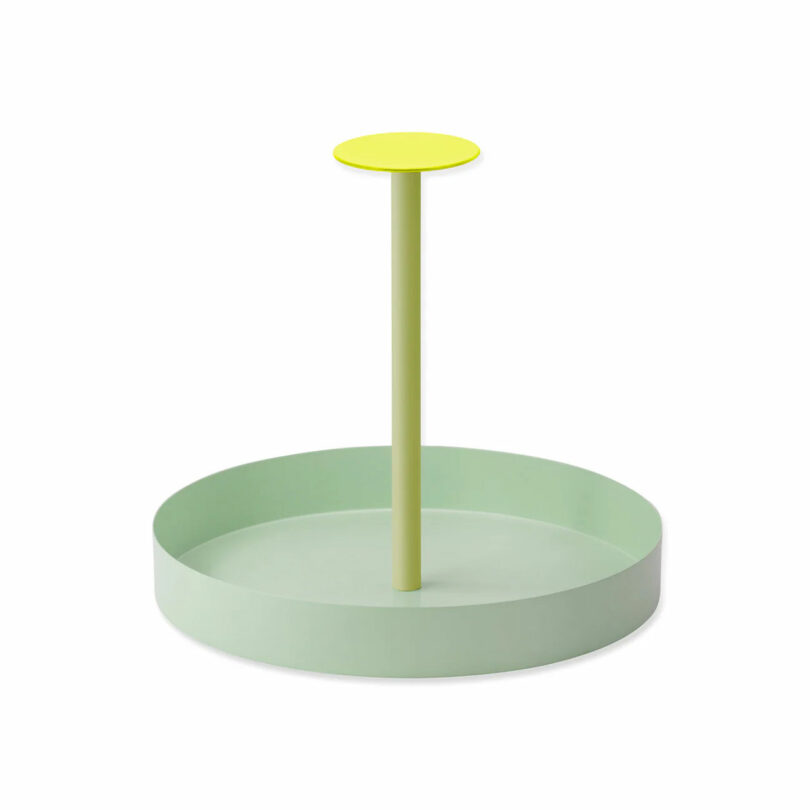 A light green round tray with a centered vertical handle and a small yellow circular top—perfect as one of those unique gifts for cooks who love stylish kitchen accessories.