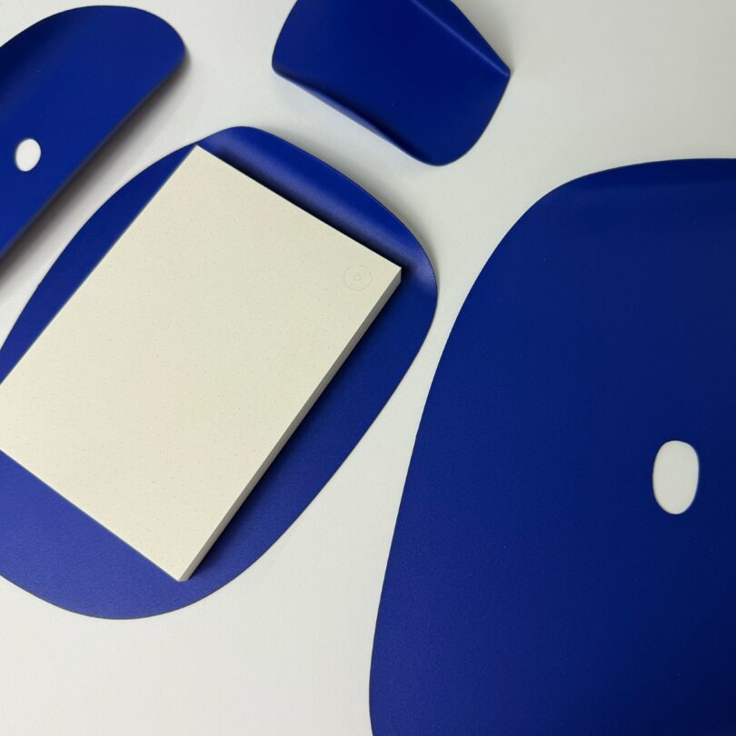 A white notepad with dotted pages sits among several flat, irregularly shaped blue objects on a white surface
