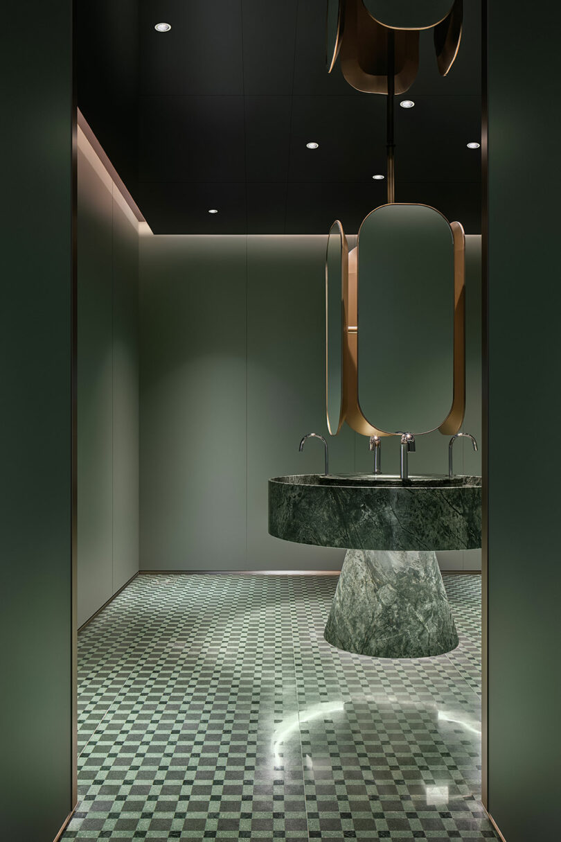 Modern bathroom with green marble pedestal sink, geometric mirrors, green checkered floor tiles, and minimalist lighting.