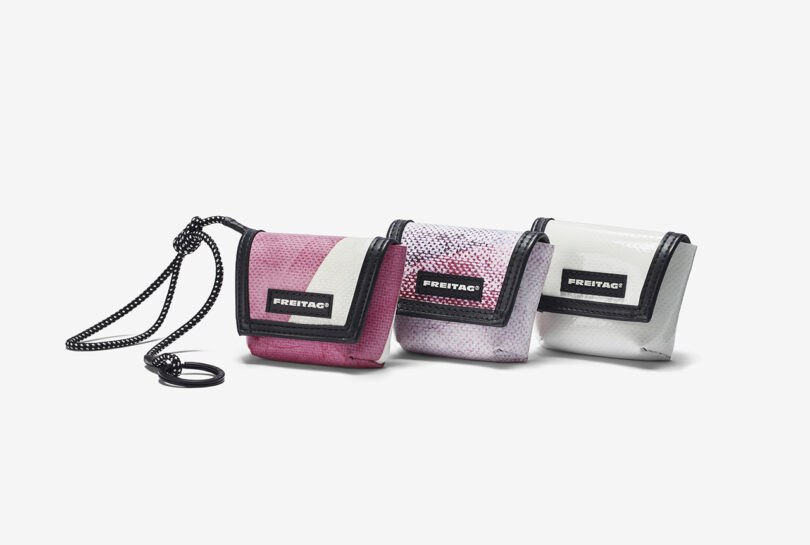 Three small FREITAG pouches in red, light purple, and white, each with a flap closure and branded label, arranged side by side on a white background.