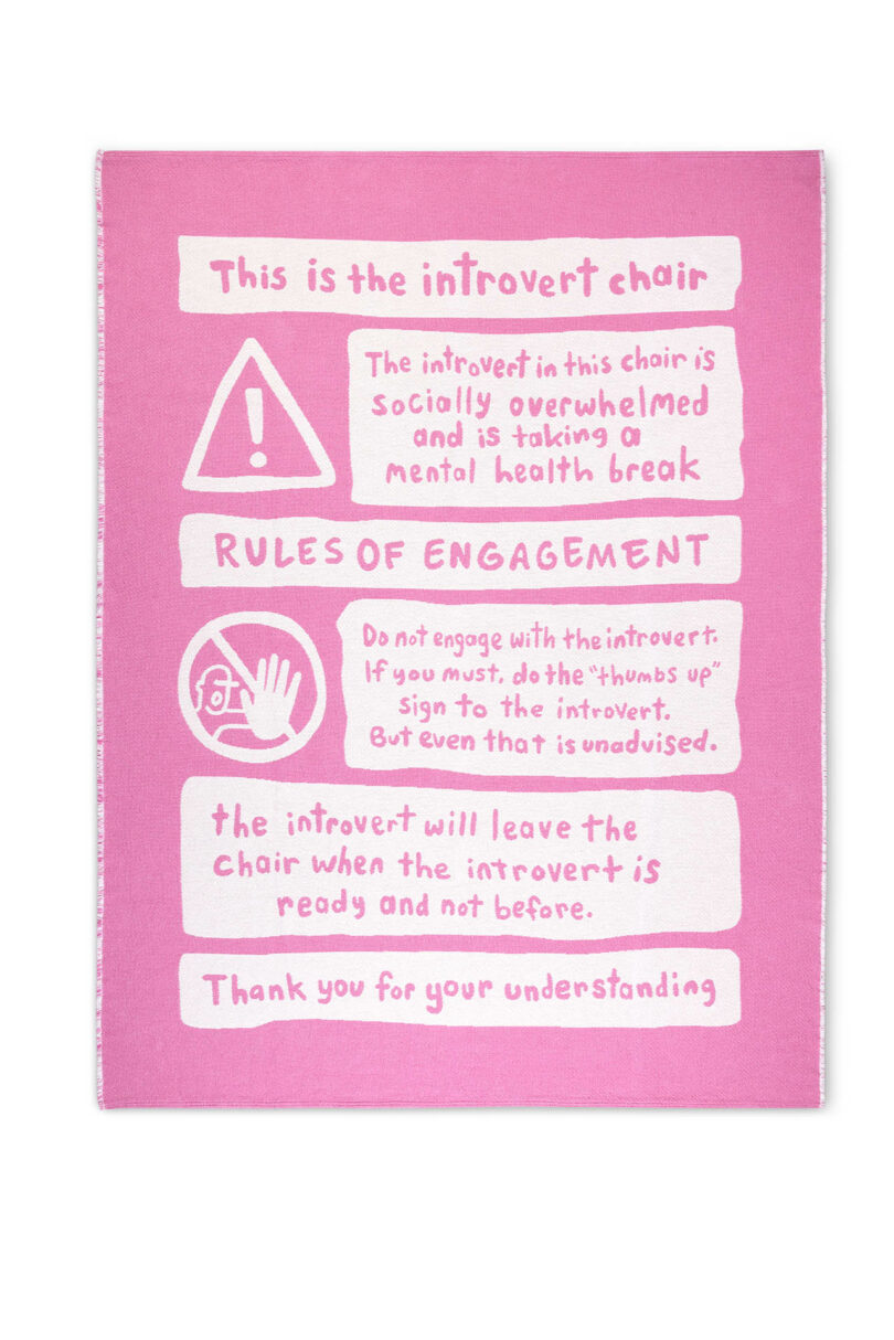 A pink blanket titled "The Introvert Chair" lists rules about using the chair for social breaks, engaging respectfully, and leaving when ready. White text and symbols illustrate the guidelines.