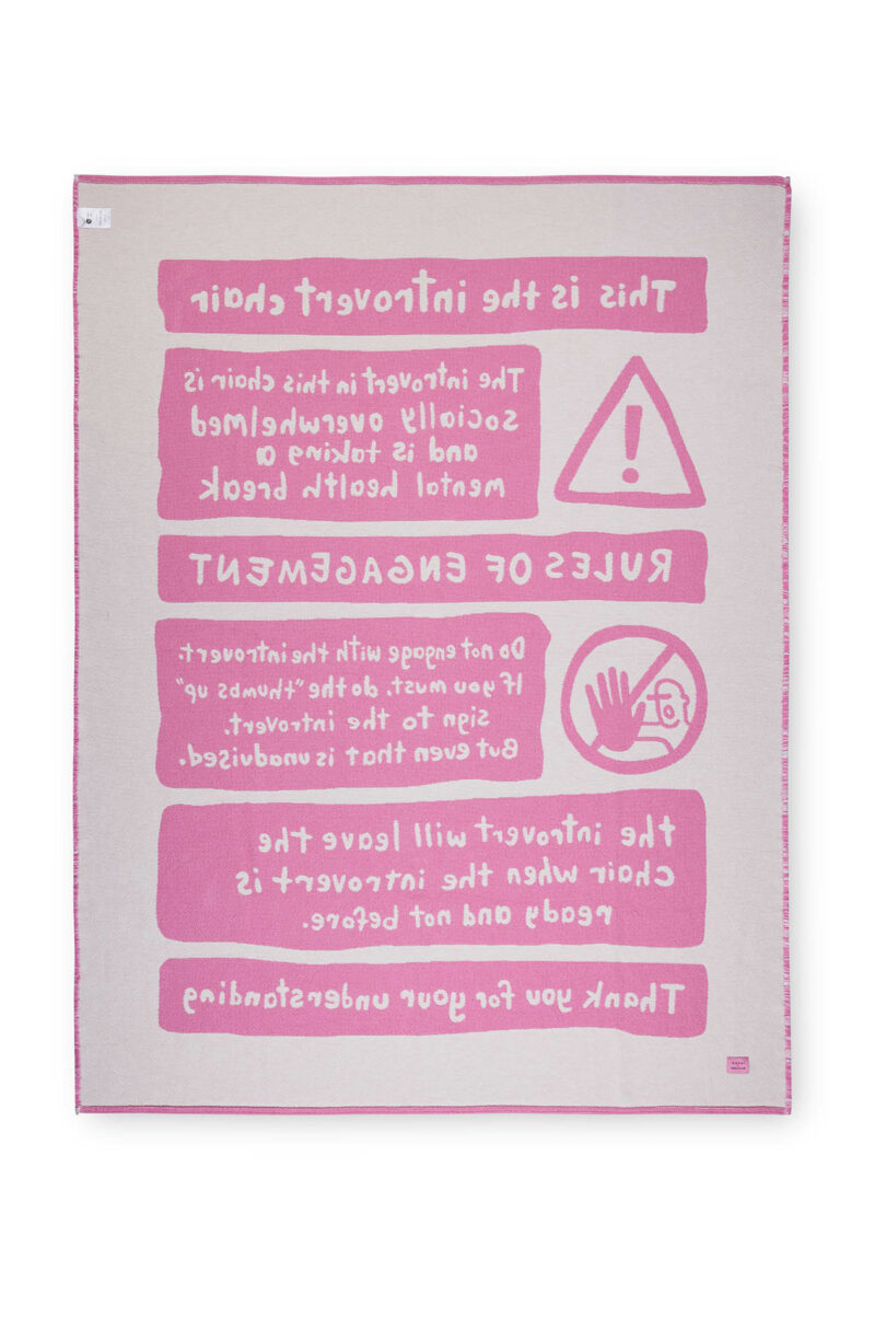 A blanket with pink text and symbols displaying "Introvert Chair" rules, including warnings about social interactions and the need for understanding.