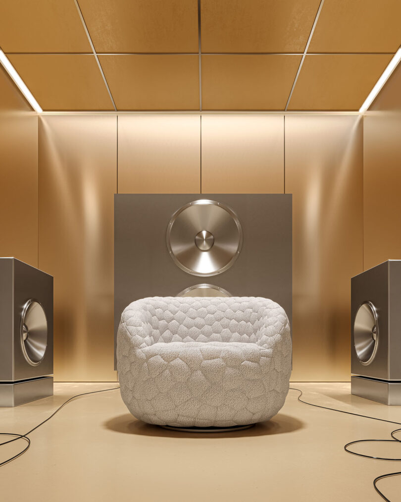 A modern room with gold walls features a textured white armchair centered in front of large silver acoustic panels and flanked by two speakers.