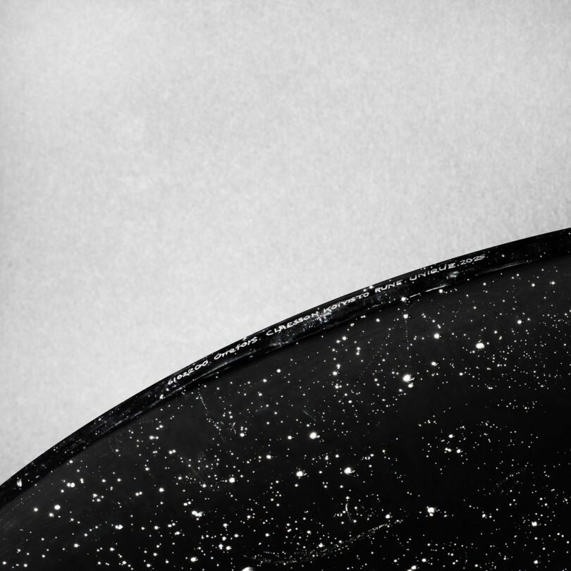 A close-up of a black circular object with white specks resembling stars, partially set against a plain light background, evokes the minimalist elegance typical of Claesson Koivisto Rune designs.