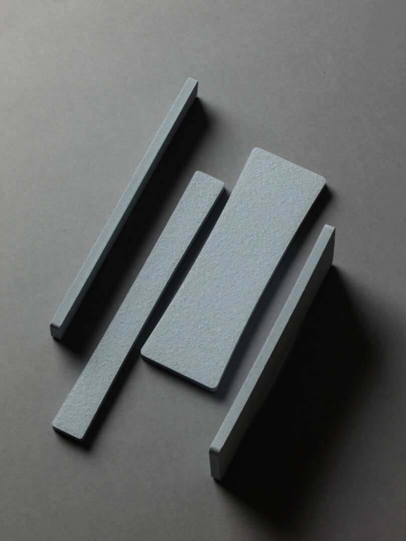 Four gray rectangular tiles are arranged on a dark gray surface, with three thin tiles parallel and one wider, angled tile in the center