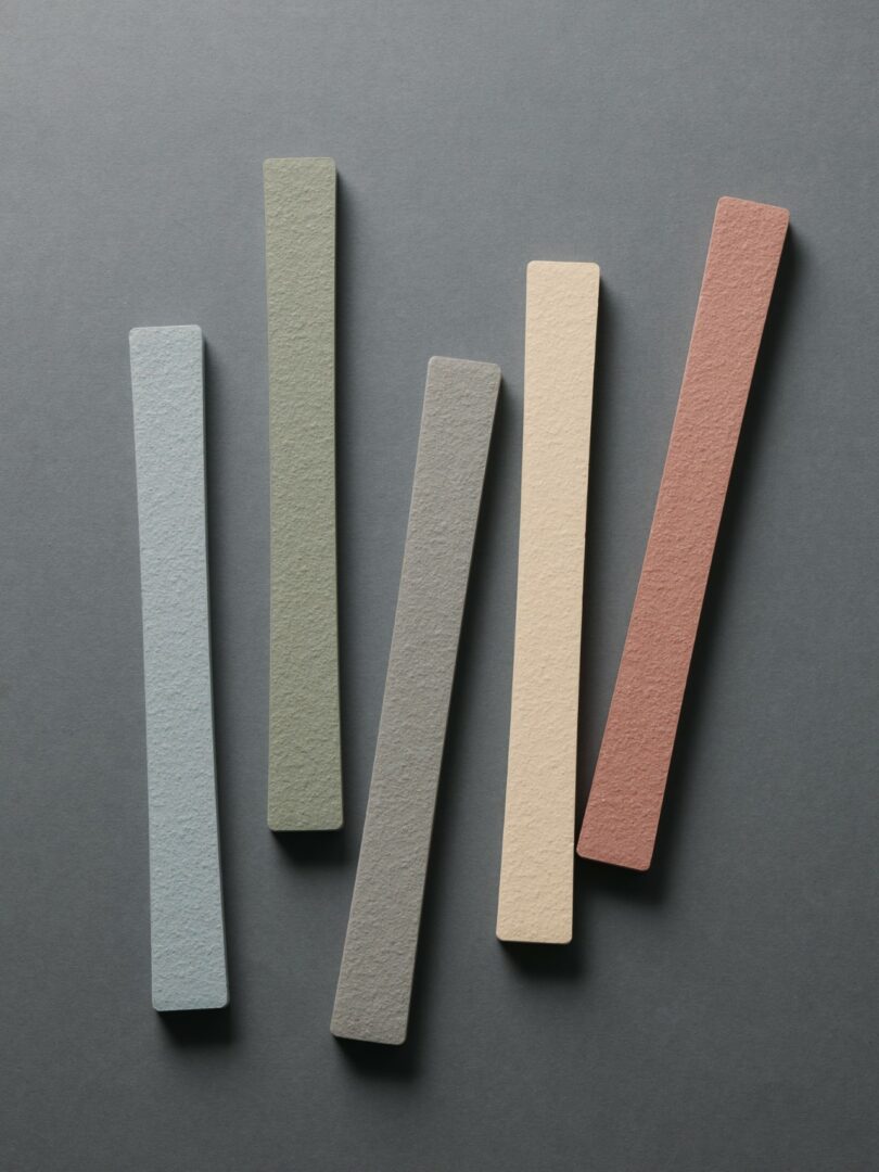 Five rectangular sticks in muted blue, green, gray, beige, and red are arranged on a dark gray background