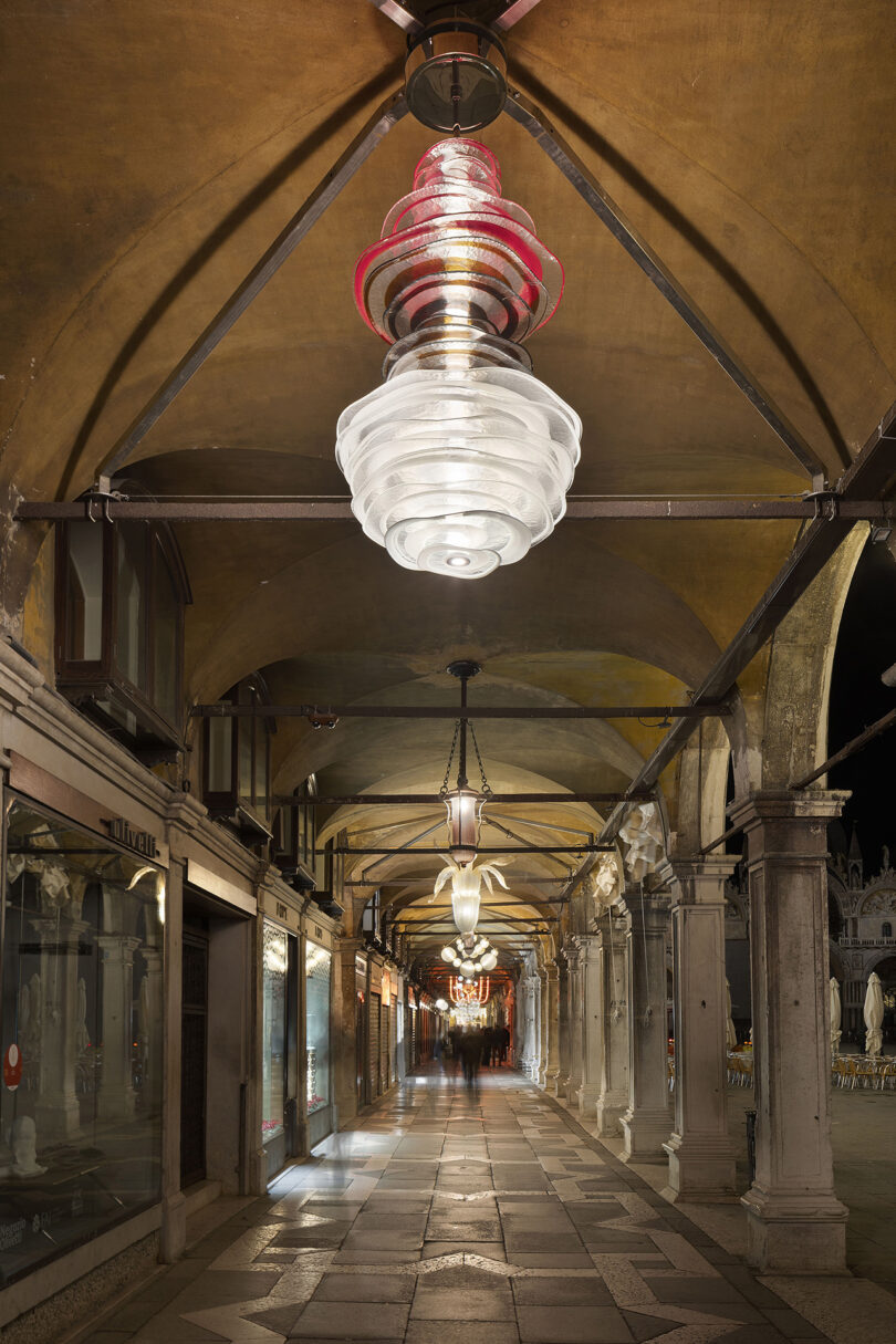 Night view of a covered walkway with arched ceilings, glass pendant lights, and closed shopfronts lining both sides.
