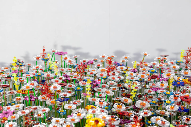 A field of colorful artificial flowers made from various materials is displayed against a plain white background.