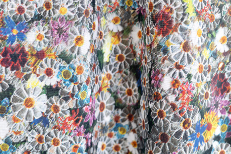 A close-up of fabric with a colorful floral pattern featuring densely packed white daisies and multicolored flowers.