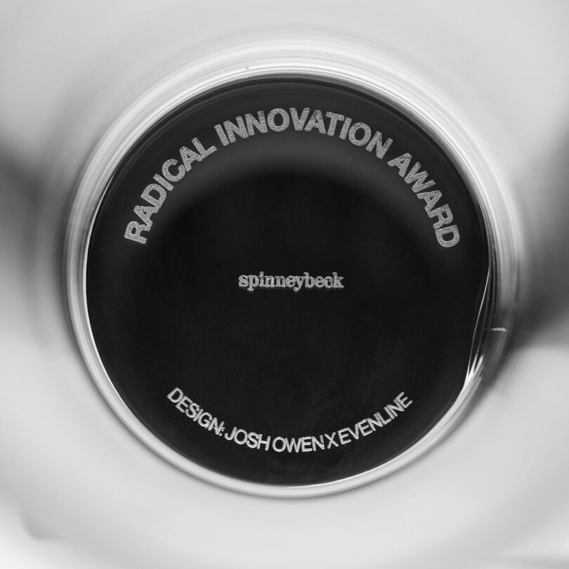 Close-up of a circular award plaque with the text "RADICAL INNOVATION AWARD," "spinneybeck," and "DESIGN: JOSH OWEN X EVENLINE.