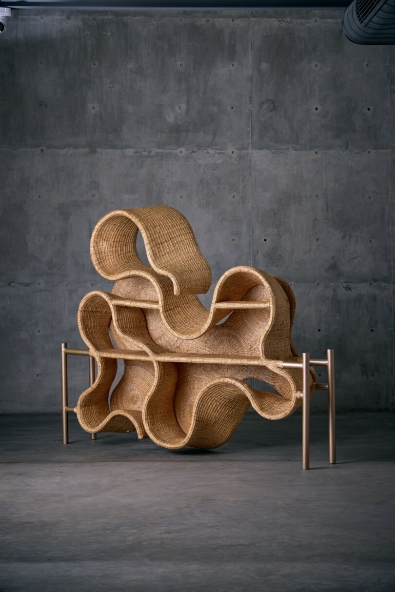 Woven rattan shelf with abstract, curving shapes, supported by a minimalist metal frame, set against a plain concrete wall