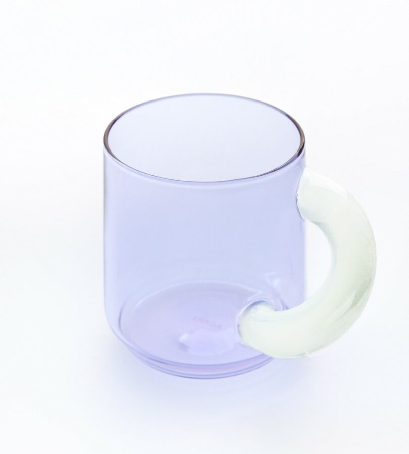 A transparent light purple glass mug with a curved, white handle, placed on a plain white background