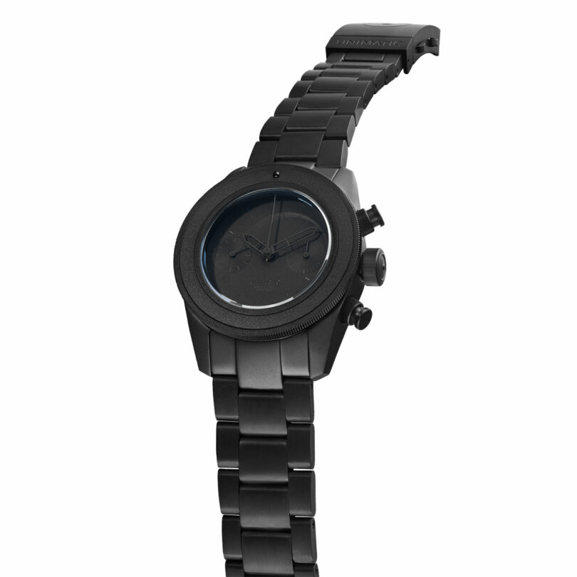 A black metal wristwatch with a partially detached band, black watch face, and two side buttons is angled against a white background.