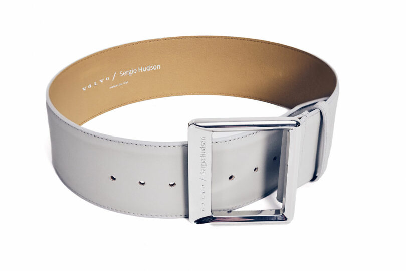 A wide, light-colored leather belt with a large, rectangular silver buckle and visible inner branding, displayed on a white background.